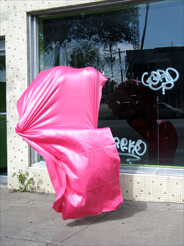 A silk-satin, hot pink mass of fabric seems similarly occupied by a body, but floats in front of a shop window, unmoored.