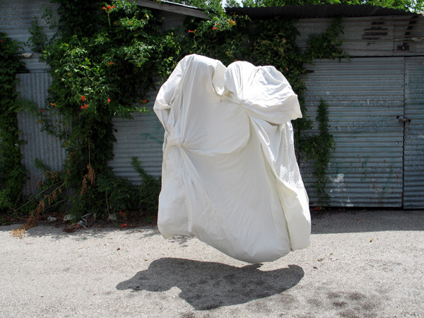 A plain cotton sheet floats above the ground, seems to be inhabited by two human bodies.