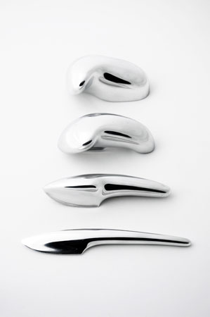 four shiny metal eating implements in a row—moving from a blunt, unformed shapes for pushing food, to the sharper precision of the familiar knife.