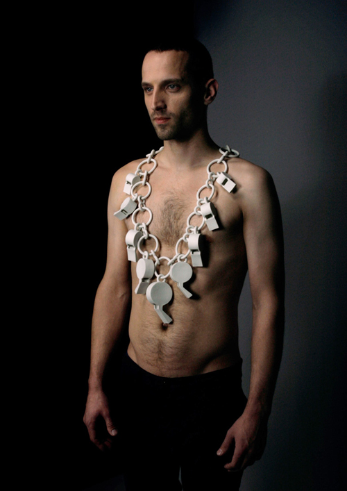 A man wears a long white porcelain necklace of eight oversize whistles, linked together by a chain.