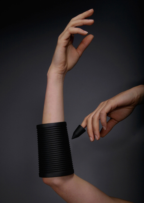 Close up of a woman wearing a guiro cuff: a corrugated porcelain bracelet, made to be stroked by a finger on the opposite hand, whose tip is capped by a porcelain "thimble"  with a pointed tip.