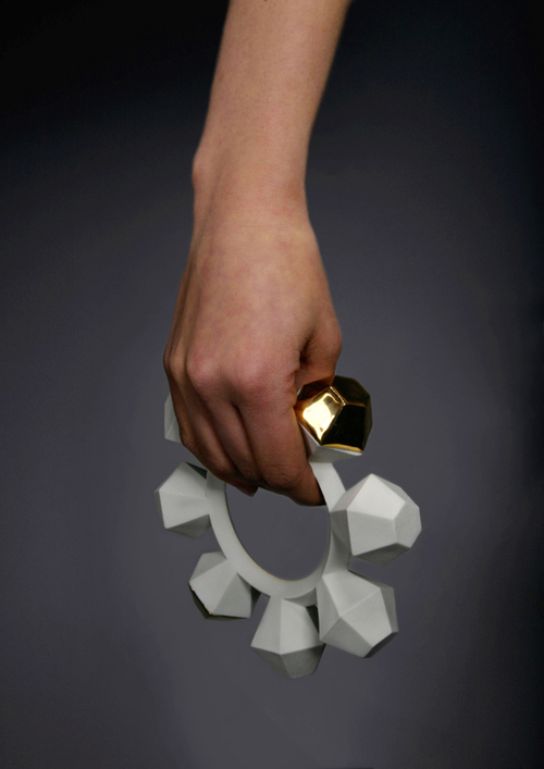 A large bangle bracelet, of porcelain, with five spokes shaped like baby rattles. One spoke is brass, like on a tambourine.