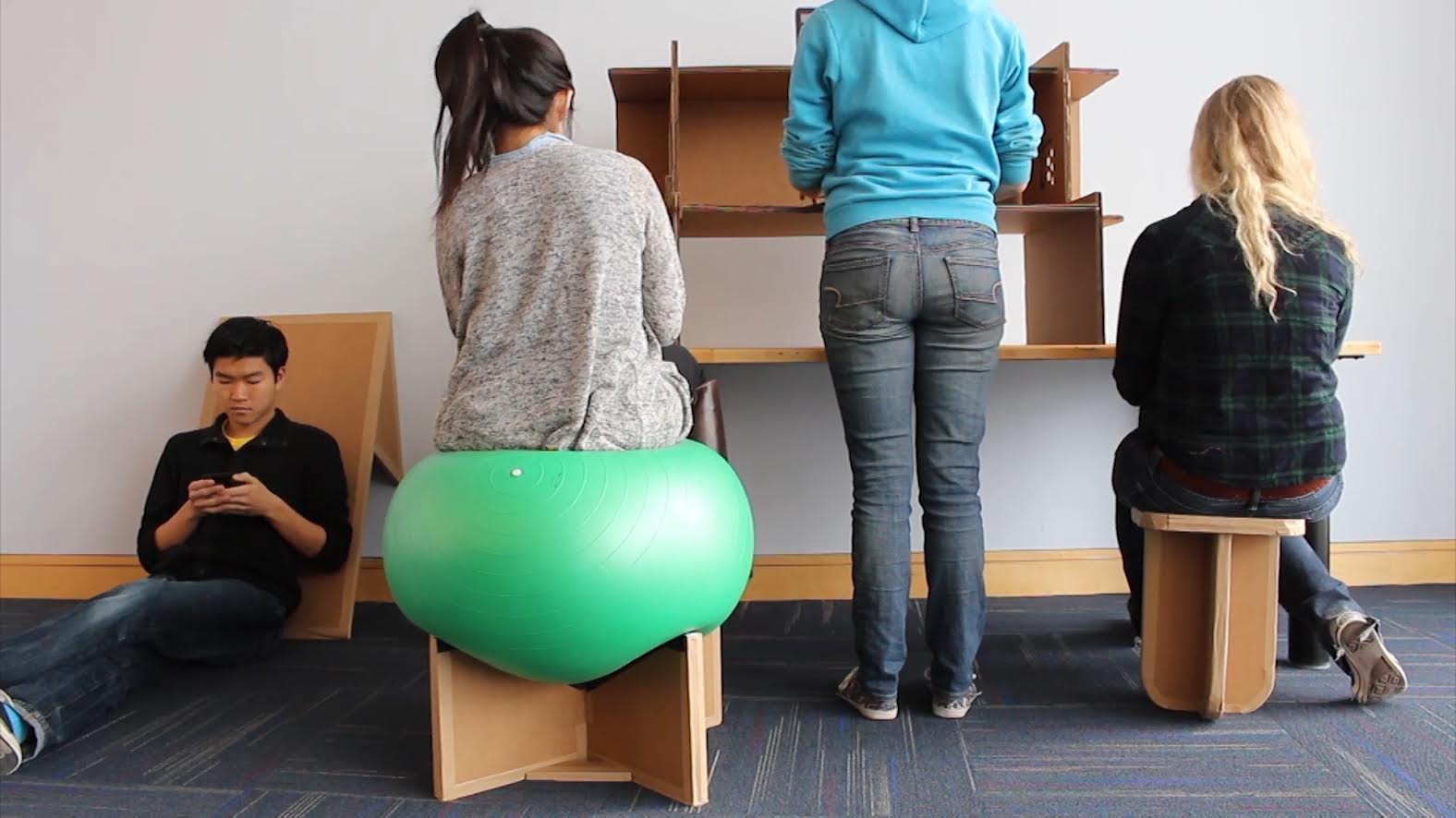 a still from a student video advertising the work of the Adaptive Design Association: four students use cardboard furniture and adaptations for study