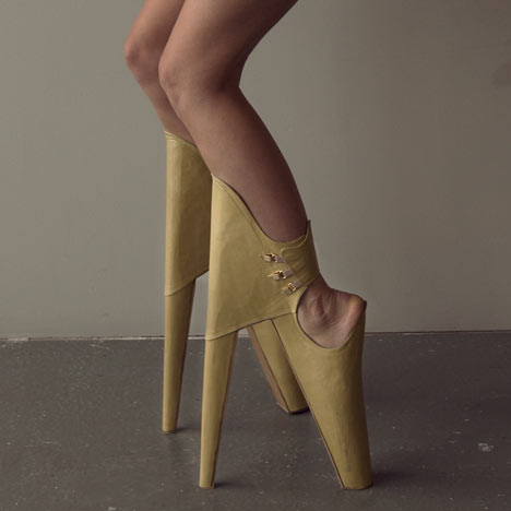 close up shot of a woman in leather "heels." The shoes have the higher heel in front, braced by the front of the calf, so the wearer must bend at an awkward angle to wear them.
