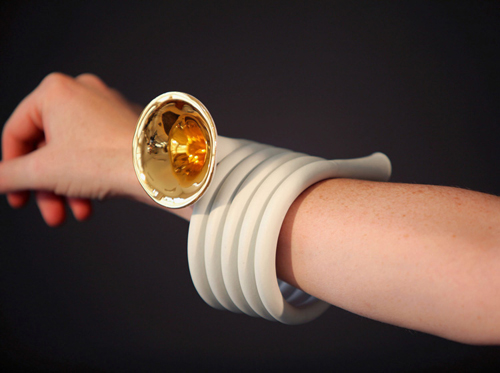 A "horn bracelet"—porcelain tubing wraps around a woman's wrist, like a coil, five rows deep. At the end of the coil is a small brass horn, like a tiny tuba.