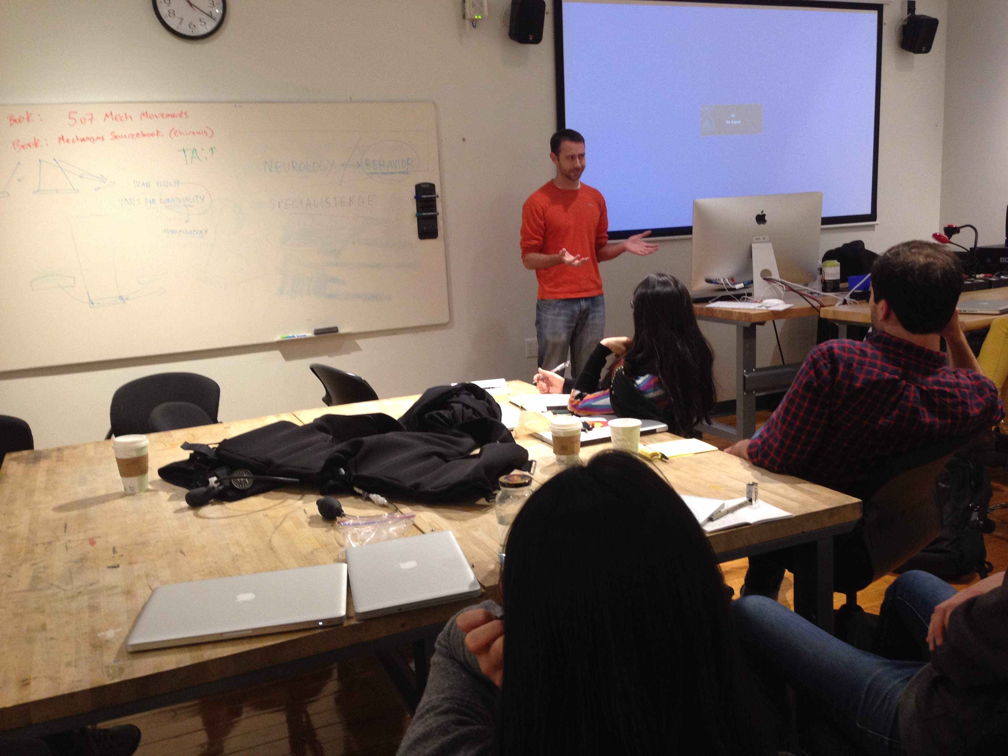 Brian Mullen speaks to my class, with students around tables watching his slides.