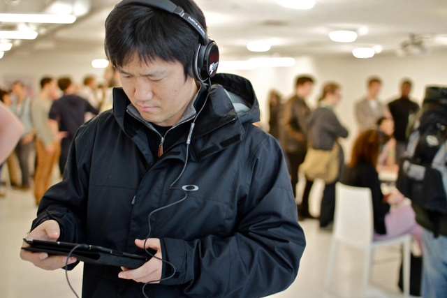 A man wears headphones and hold an iPad, listening to the aural game.