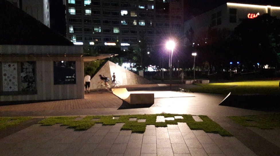 A nighttime view of the ramps at Buk Seoul museum site, with three young adults riding the ramps after hours.