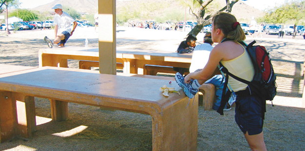 A woman uses a waist-high picnic bench to prop her foot so she can tie her shoe.